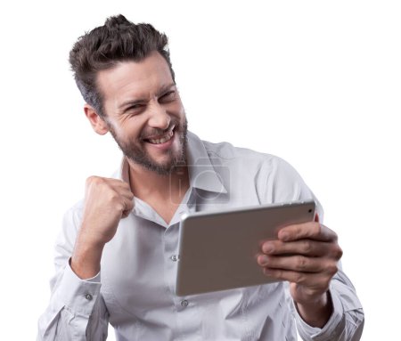 Foto de Alegre hombre sonriente recibiendo buenas noticias en la tableta con el puño levantado - Imagen libre de derechos