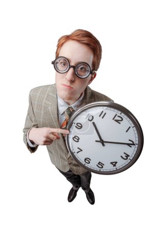 Foto de Divertido chico nerd con gafas gruesas sosteniendo un reloj, él está enojado y decepcionado, plazos concepto - Imagen libre de derechos