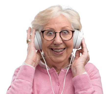 Téléchargez les photos : Heureuse femme âgée portant un casque et écoutant de la bonne musique, elle est joyeuse et appréciant - en image libre de droit