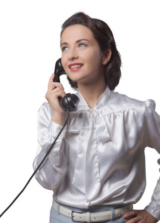 Foto de Atractiva secretaria vintage elegante que tiene una llamada telefónica y sonriendo - Imagen libre de derechos
