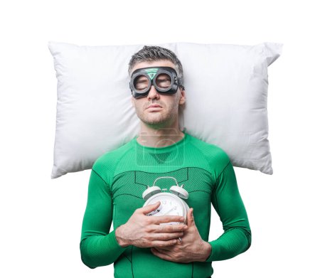 Photo for Superhero sleeping on a pillow floating in the air holding alarm clock. - Royalty Free Image