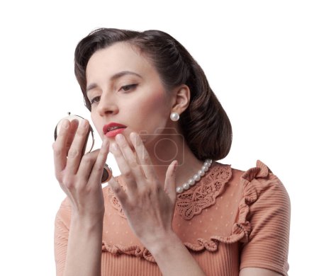 Téléchargez les photos : Élégante femme de style vintage qui se regarde dans le miroir, elle retouche son maquillage - en image libre de droit