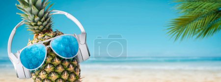 Funny pineapple wearing headphones and sunglasses at the tropical beach, summer vacations and party concept, copy space