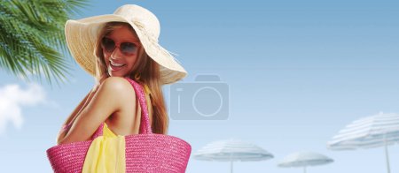 Photo for Beautiful smiling young woman at the beach resort, she is carrying a beach bag, summer vacations concept - Royalty Free Image