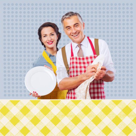 Téléchargez les photos : Couple vintage souriant dans un tablier vaisselle lavage ensemble - en image libre de droit