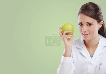 Photo for Professional female nutritionist holding a green apple and smiling, diet and healthy eating concept, copy space - Royalty Free Image
