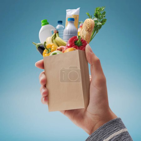Photo for Customer holding a miniature paper bag with fresh groceries falling inside, grocery shopping concept - Royalty Free Image