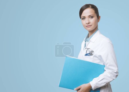 Photo for Smiling young female doctor holding medical records file. - Royalty Free Image