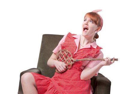 Téléchargez les photos : Drôle rétro femme au foyer chantant et tenant un batteur de tapis comme si c'était une guitare, elle s'ennuie et paresseuse - en image libre de droit