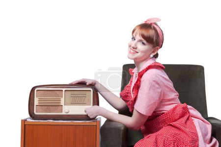 Estereotipado estilo vintage ama de casa sentada en la sala de estar y escuchando música, ella está sintonizando la radio