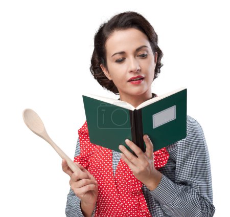 Photo for Smiling vintage woman holding an open cookbook and a wooden spoon - Royalty Free Image