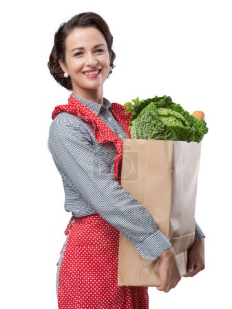 Foto de Mujer vintage sonriente en delantal sosteniendo una bolsa de compras
. - Imagen libre de derechos