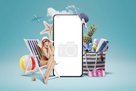 Photo for Beautiful young woman lying on a deckchair and sunbathing next to a big smartphone with blank screen, bag with beach accessories: book your summer vacation online - Royalty Free Image