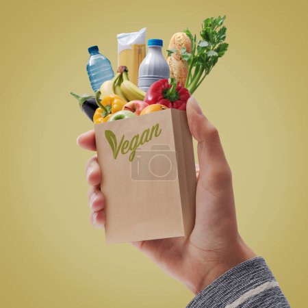 Téléchargez les photos : Femme tenant un mini sac d'épicerie complet avec des produits végétaliens sains - en image libre de droit