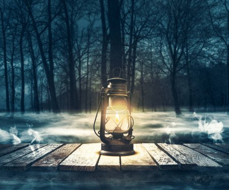 Foto de Linterna de luz en una cubierta de madera y bosque brumoso, horror y misterio concepto - Imagen libre de derechos