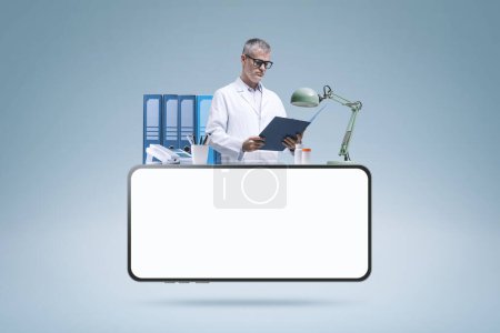 Foto de Médico profesional trabajando en su consultorio y smartphone con pantalla en blanco: telemedicina y concepto de médico en línea - Imagen libre de derechos