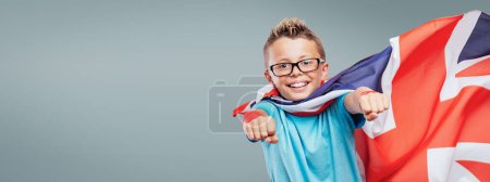 Téléchargez les photos : Super héros britannique souriant portant un drapeau comme une cape et volant avec les poings levés - en image libre de droit
