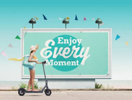 Photo for Happy woman riding an e-scooter and going to the beach, motivational poster in the background: enjoy every moment - Royalty Free Image