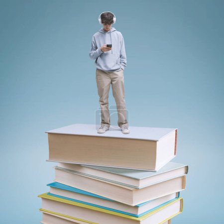 Téléchargez les photos : Jeune écolier utilisant un smartphone et debout sur une pile de livres : concept d'apprentissage et d'éducation en ligne - en image libre de droit