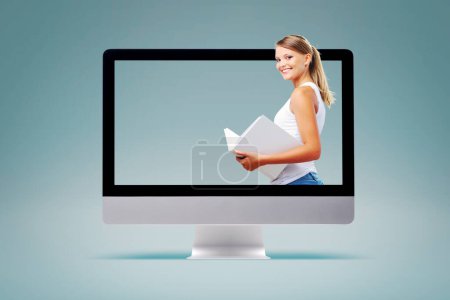 Photo for Happy young student holding a book in a computer screen, e-learning and online courses concept - Royalty Free Image