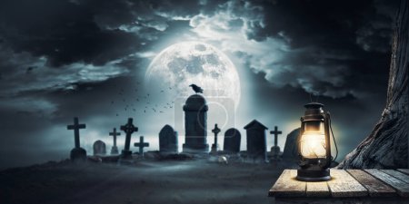 Téléchargez les photos : Cimetière effrayant avec des tombes anciennes et une vieille lanterne allumée au premier plan - en image libre de droit