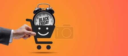 Téléchargez les photos : Client tenant une icône panier avec réveil à l'intérieur : achats en ligne et concept de vente Black Friday - en image libre de droit