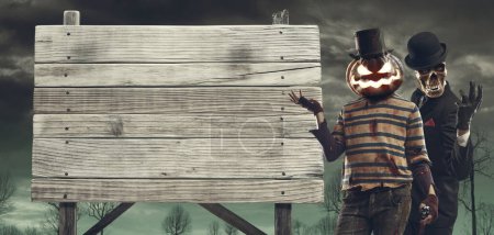 Foto de Espeluznantes personajes de Halloween mostrando un viejo signo de madera en blanco - Imagen libre de derechos