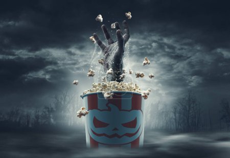 Foto de Mano de zombie asustadiza saliendo de un cubo de palomitas de maíz: películas de terror y concepto de Halloween - Imagen libre de derechos