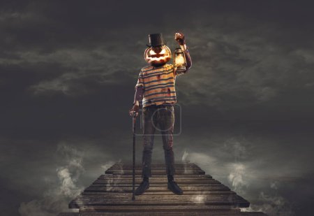 Téléchargez les photos : Monstre effrayant Halloween avec tête de citrouille debout sur une terrasse en bois et tenant une lanterne - en image libre de droit