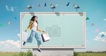 Photo for Large billboard with copy space and happy woman holding shopping bags, sale and offers concept - Royalty Free Image