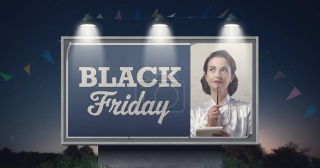Téléchargez les photos : Vente promotionnelle vendredi noir annonce avec femme vintage souriante écrivant une liste d'achats - en image libre de droit