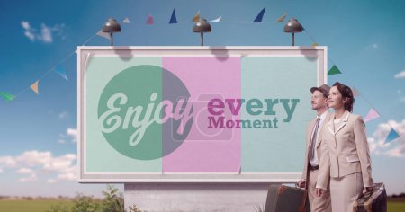 Photo for Vintage style couple traveling together and motivational quote on billboard: enjoy every moment - Royalty Free Image