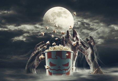 Téléchargez les photos : Seau de maïs soufflé entouré de mains de zombies et de pleine lune : films d'horreur et concept d'Halloween - en image libre de droit