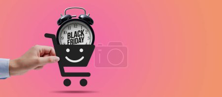 Téléchargez les photos : Client tenant une icône panier avec réveil à l'intérieur : achats en ligne et concept de vente Black Friday - en image libre de droit
