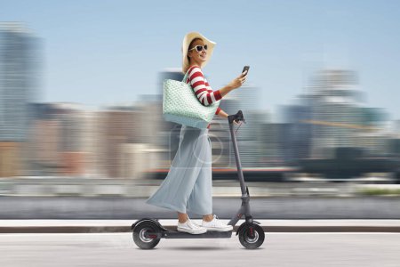 Foto de Mujer distraída montando un scooter eléctrico rápido y charlando con su teléfono inteligente - Imagen libre de derechos