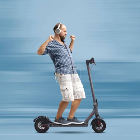 Téléchargez les photos : Homme joyeux écoutant de la musique et dansant tout en conduisant un scooter électrique rapide - en image libre de droit