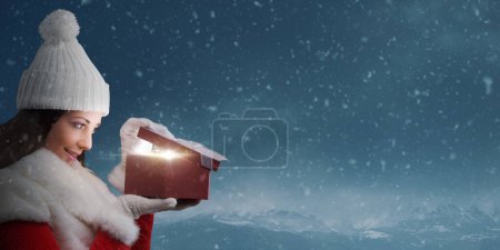 Foto de Mujer Santa Claus abriendo un regalo de Navidad, hay una hermosa sorpresa dentro de la caja, cielo nevado en el fondo - Imagen libre de derechos