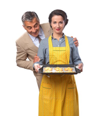 Photo for Vintage happy couple smiling, she is serving home made gingerbread men cookies - Royalty Free Image