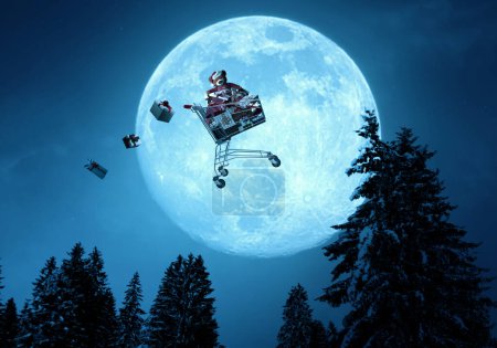 Foto de Carro de compras mágico lleno de regalos volando en el cielo nocturno en Nochebuena - Imagen libre de derechos