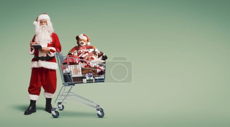 Téléchargez les photos : Père Noël écrivant une liste et un panier plein de cadeaux, concept d'achat de Noël - en image libre de droit