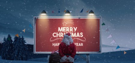 Foto de Santa Claus leyendo los deseos de Navidad en un cartel debajo de la nieve - Imagen libre de derechos
