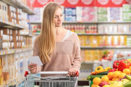 Photo for Attractive young woman pushing a shopping cart and buying groceries at the supermarket - Royalty Free Image