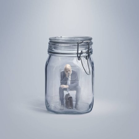 Foto de Hombre de negocios superior sin esperanza atrapado dentro de un frasco de vidrio, él está sentado y pensando, el aislamiento y el concepto de fracaso - Imagen libre de derechos