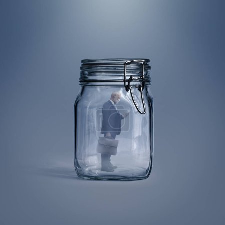Photo for Corporate businessman trapped inside a glass jar, he is using a smartphone - Royalty Free Image