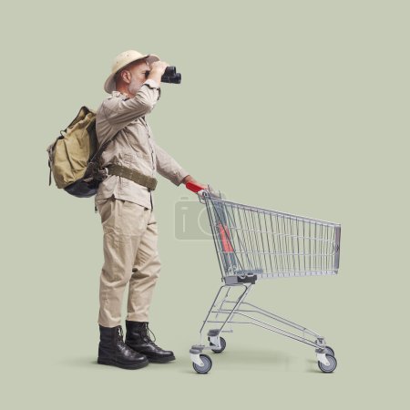 Téléchargez les photos : Aventurier senior faisant des courses, il pousse un chariot et tient des jumelles - en image libre de droit