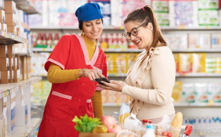 Foto de Mujer haciendo compras en el supermercado, ella está mostrando su teléfono inteligente al asistente de la tienda y pidiendo ayuda - Imagen libre de derechos