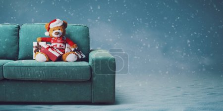 Foto de Lindo oso de peluche con sombrero de Santa en el sofá y la nieve cayendo, vacaciones y celebraciones concepto - Imagen libre de derechos