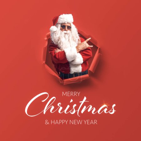 Téléchargez les photos : Mauvais Père Noël non conventionnel surgissant d'un trou dans le papier et souhaits de Noël - en image libre de droit