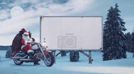 Foto de Santa no convencional que monta una motocicleta y tablero de publicidad en blanco, concepto de campaña publicitaria de Navidad - Imagen libre de derechos