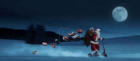 Téléchargez les photos : Père Noël contemporain chevauchant un scooter la nuit de la veille de Noël et portant des cadeaux, bannière avec espace de copie - en image libre de droit